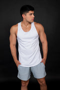 "Hombre atlético de frente vistiendo un tank top blanco de malla técnica con textura microperforada. La prenda tiene un cuello redondo y sisas amplias, combinada con shorts gris claro. El diseño resalta la musculatura de los brazos y hombros sobre un fondo negro, evocando una estética de jugador de basketball profesional".